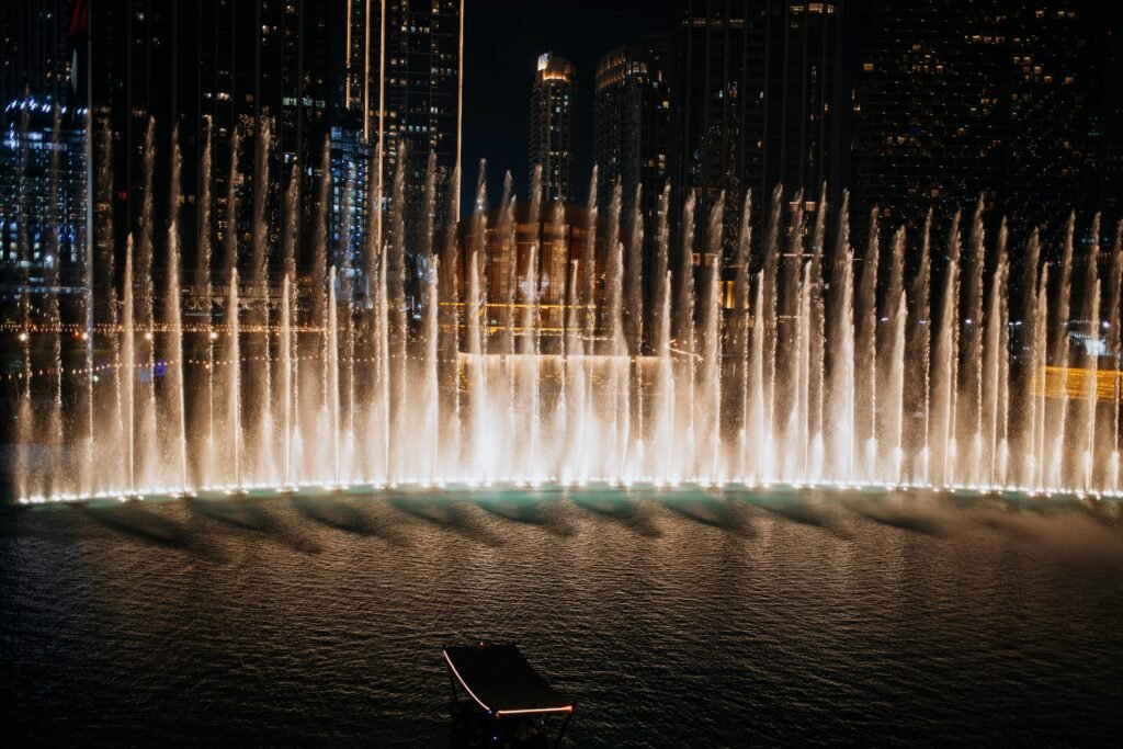 Illuminated water fountain show at night in downtown Dubai, surrounded by skyscrapers.